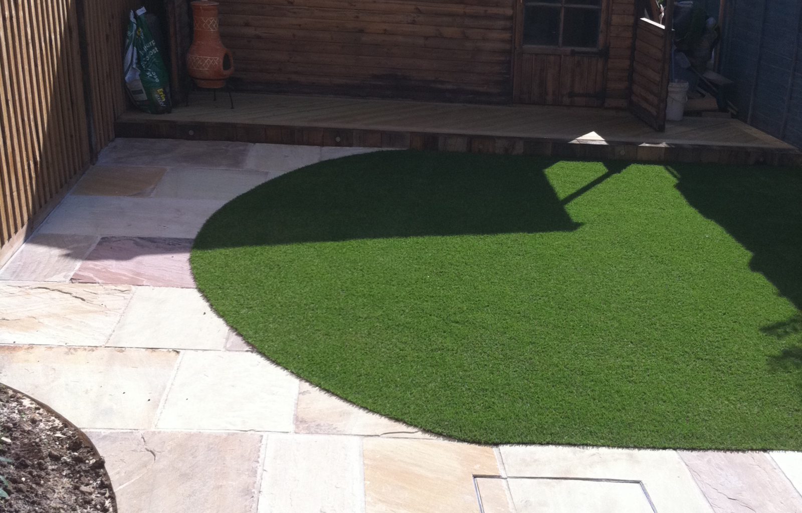 Small garden with patio area and artificial turf leading to garden room