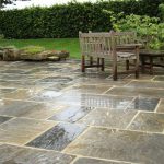 A patio area with seating area and planted containers. Lawn area and hedge in background.