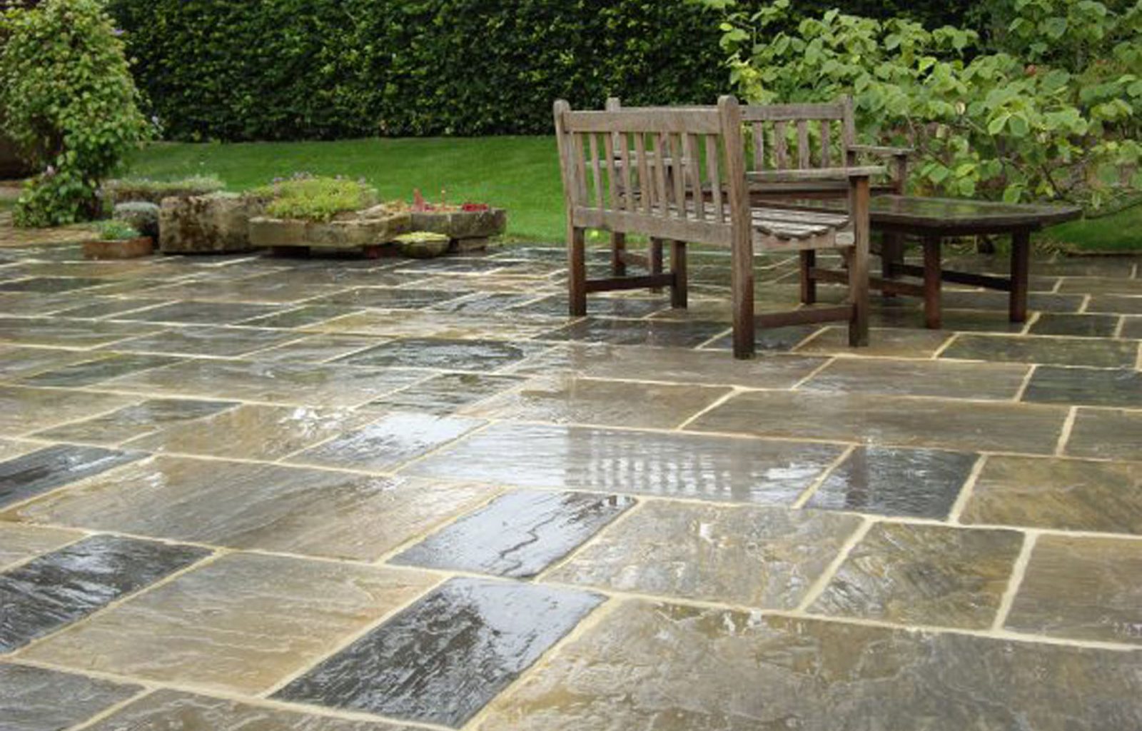 A patio area with seating area and planted containers. Lawn area and hedge in background.