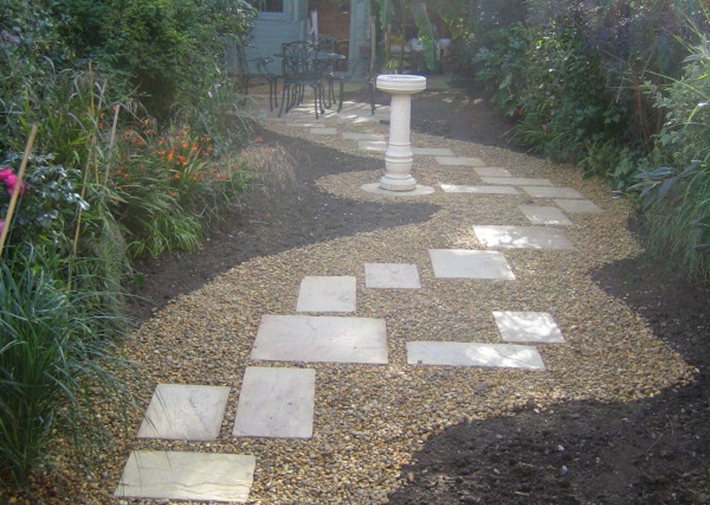 Rear garden with shingled pathway and paving stepping stones to access seating area and summer house