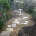 Rear garden with shingled pathway and paving stepping stones to access seating area and summer house