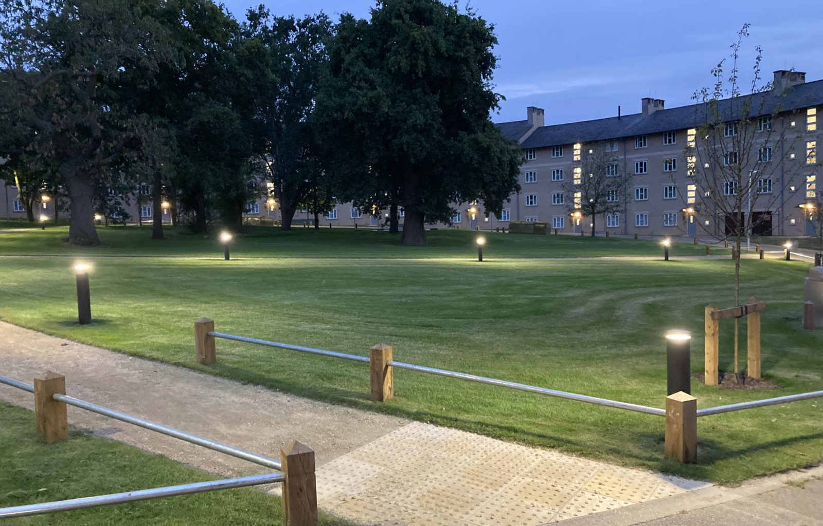 Landscaped area outside student accommodation, which features pathway lighting, mature and young trees, knee-rail fencing and accessibility paving.