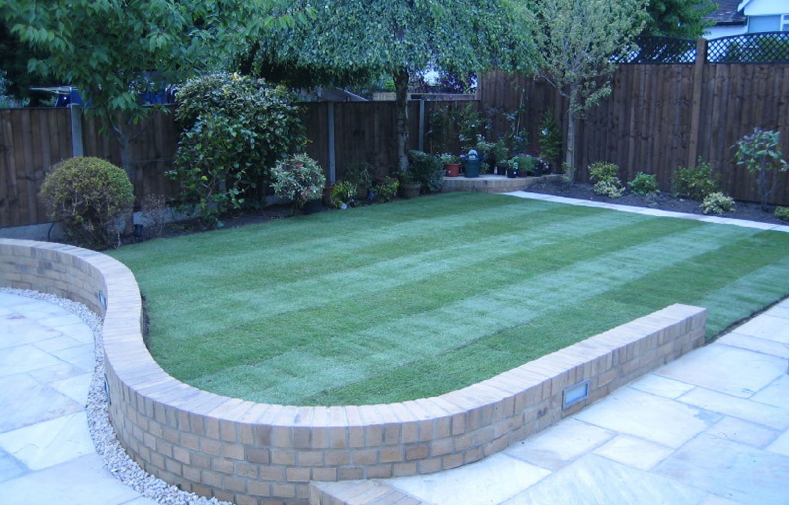 Rear garden with enclosed fencing, planted borders, freshly laid lawn, wall and paved pathway