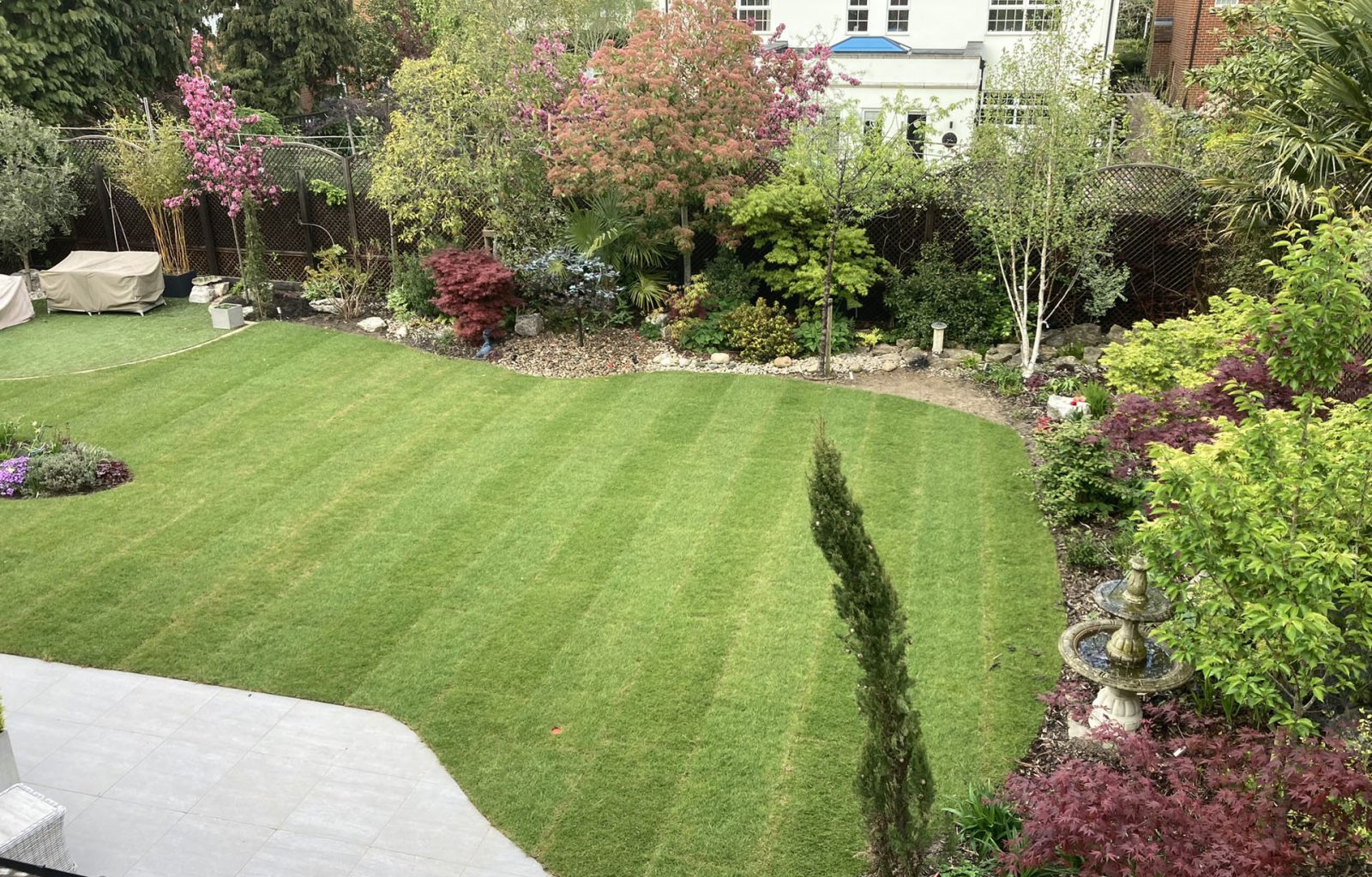 Newly laid turf with surrounding mature planted borders and patio area