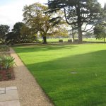 A large lawn area in front of mature trees and sports field in background