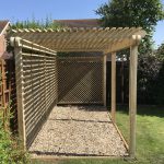 Wooden pergola with side trellis panels over a gravel base for garden seating