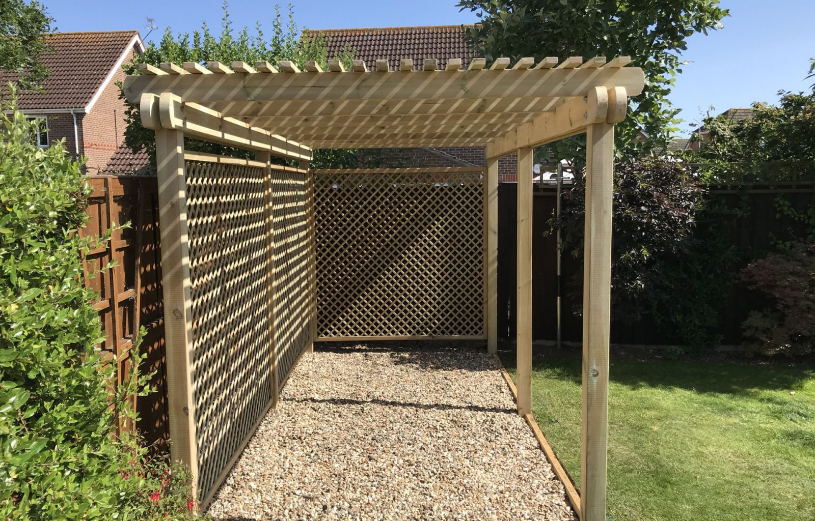 Wooden pergola with side trellis panels over a gravel base for garden seating