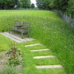 A fenced paddock area containing a natural pond, wooden bench and wildflower turf area